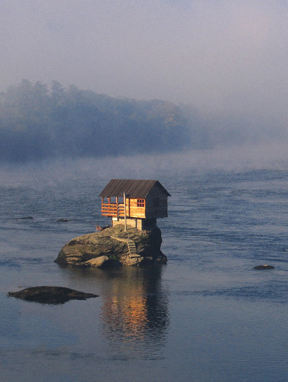 allein stehendes Haus in mitten eines Flusses mit Nebel im Hintergrund und einer refelktion im Wasser, Symbolbild für Meier & Partner Immobilien.